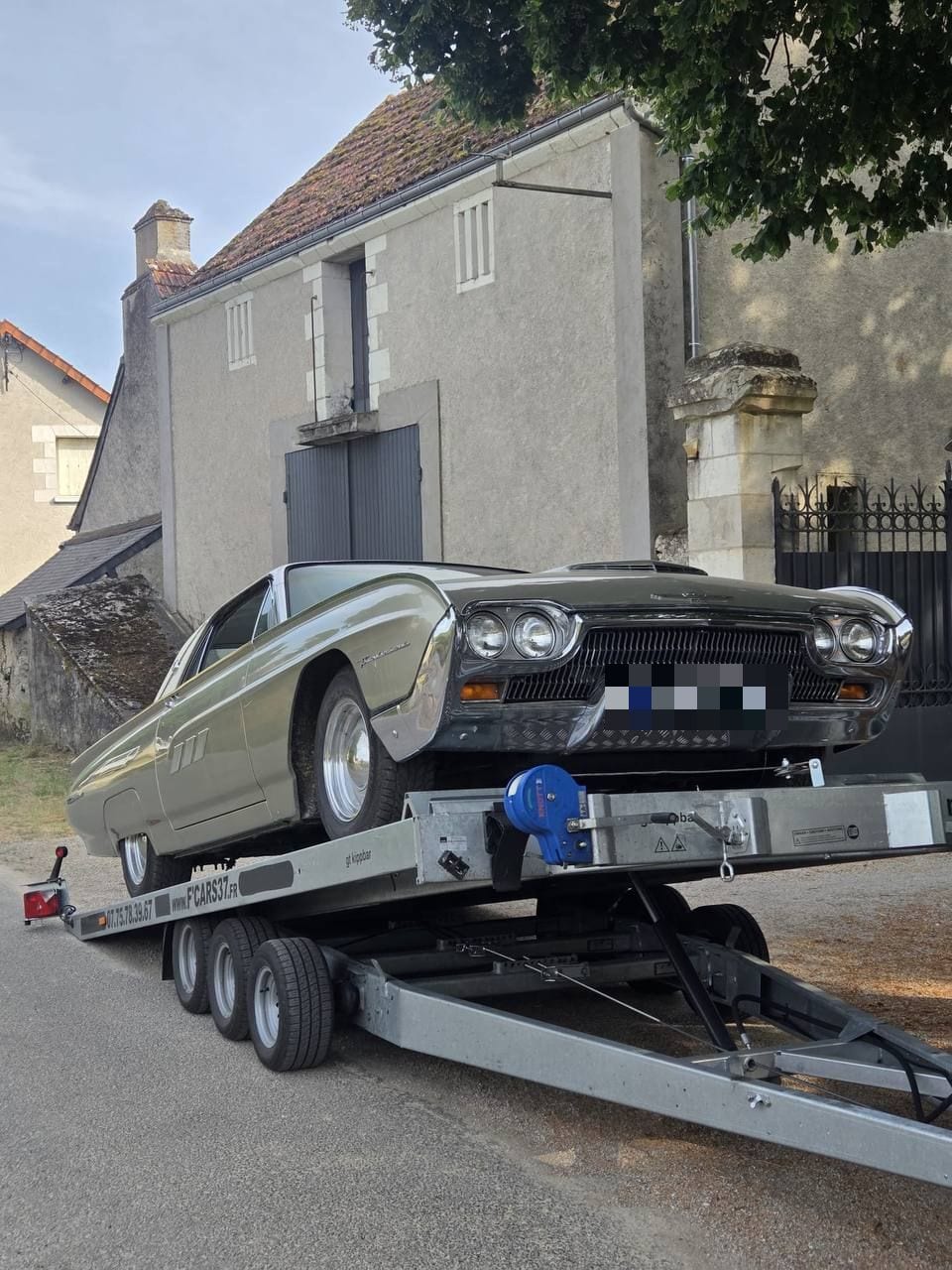Ford Thunderbird de collection chargée sur un plateau basculant dans une rue de village