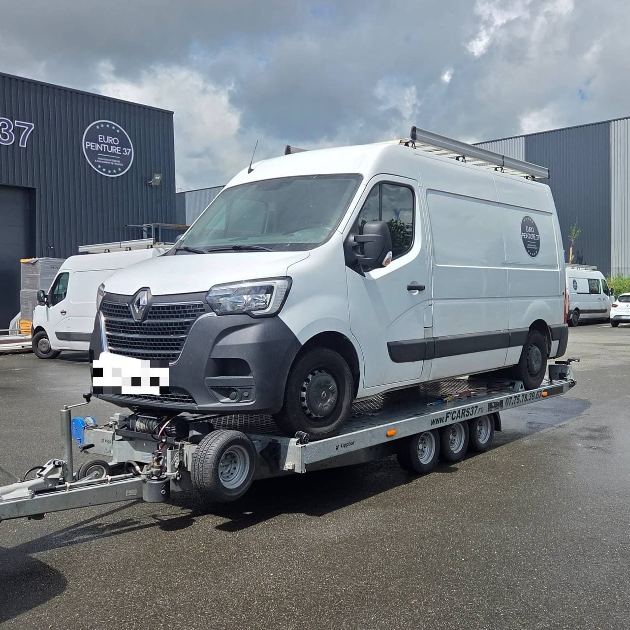 Fourgon Renault Master blanc chargé sur une remorque porte-voiture devant les locaux d'une entreprise