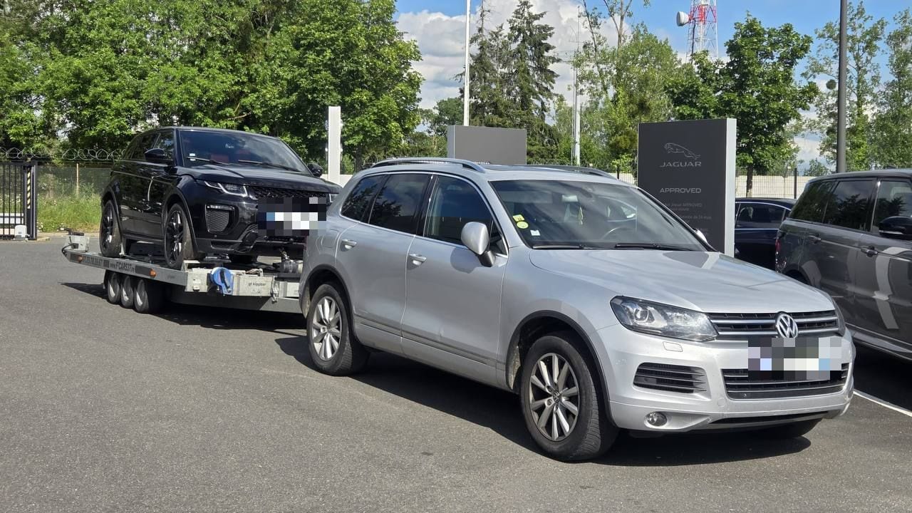 Range Rover Evoque noir sur une remorque plateau attelée à un véhicule tracteur, devant une concession automobile