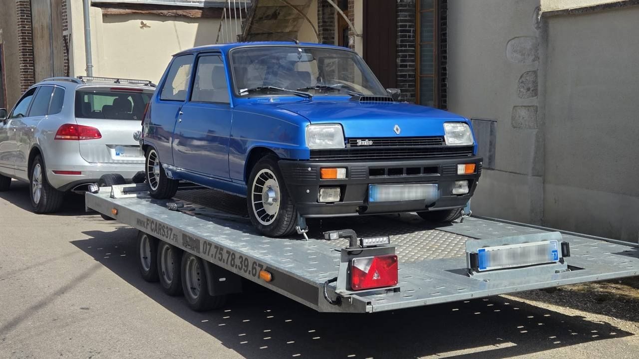 Renault 5 Alpine Turbo bleue de collection sanglée sur une remorque plateau dans une rue de village